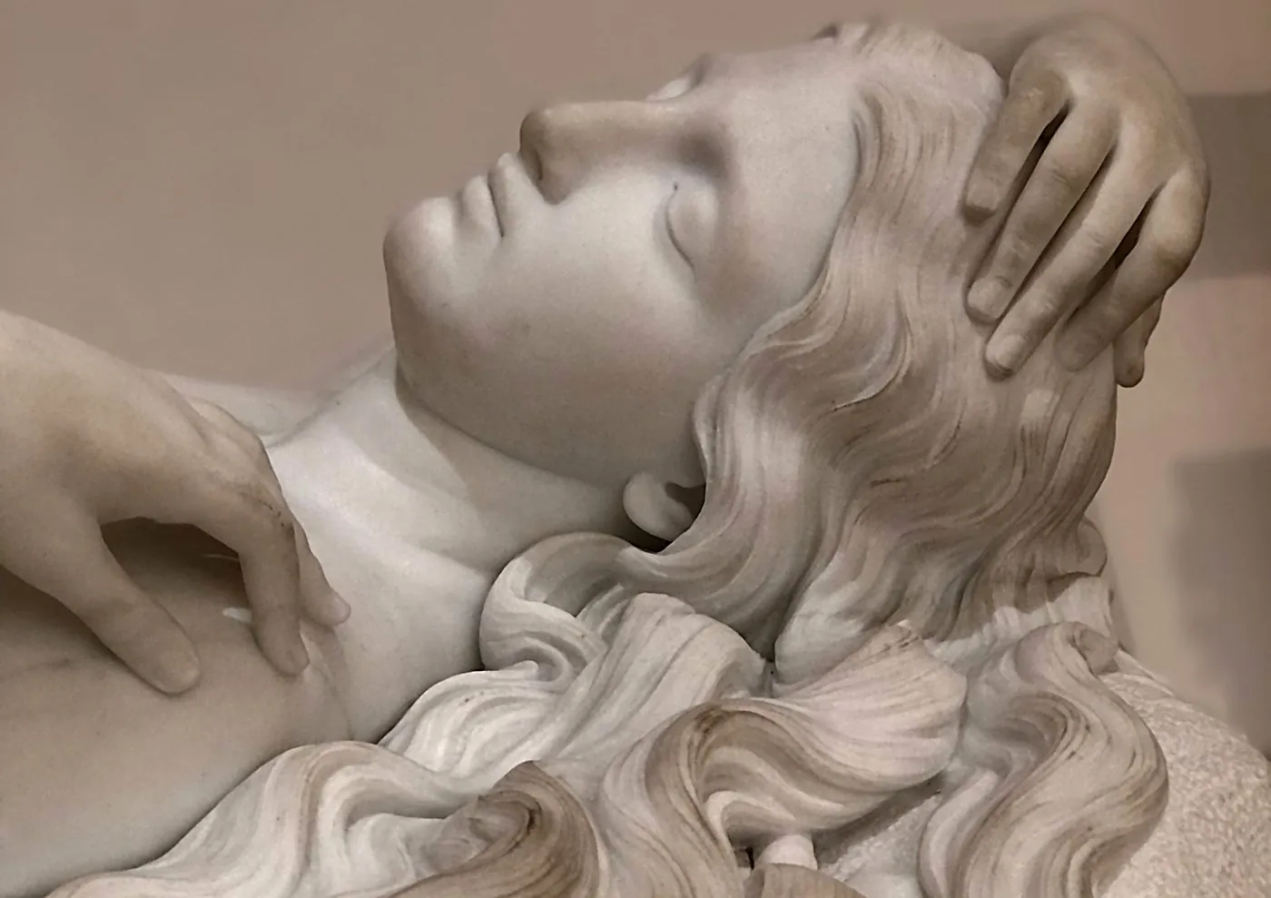 Escultura de mármol: rostro de mujer recostada con el cabello ondulado