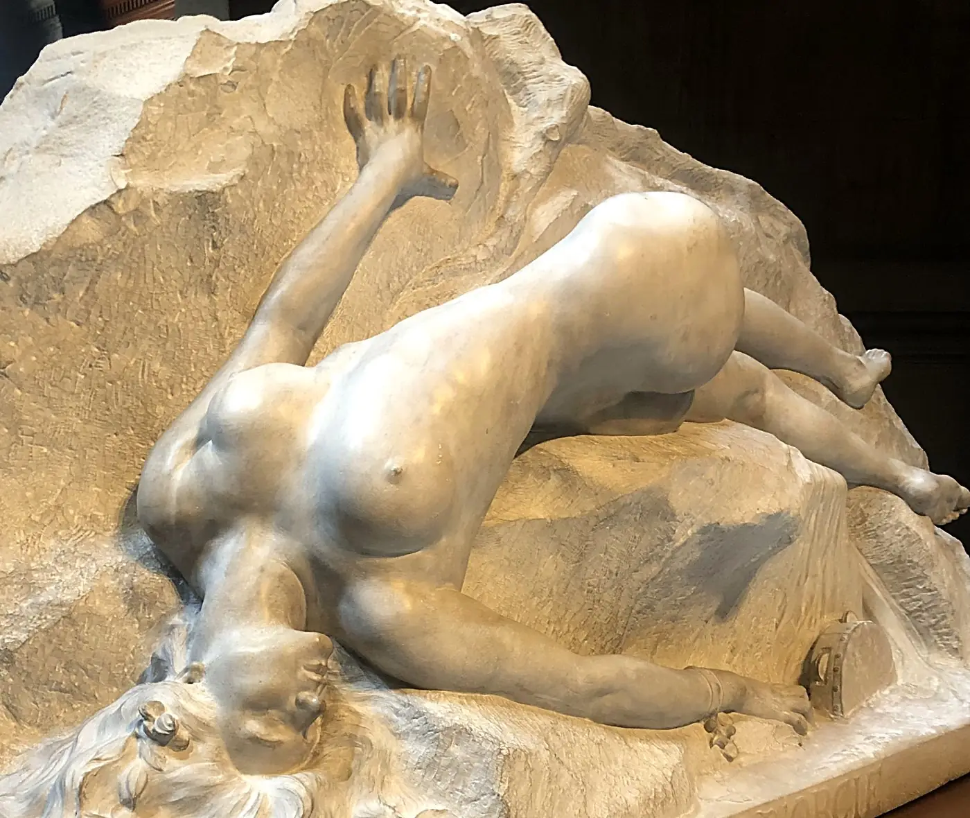 Escultura de mármol: figura femenina recostada sobre la roca